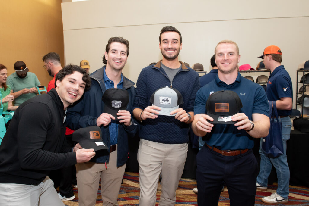 Four smiling event guests holding the custom patch hats they built at The Hat Bar of Georgia