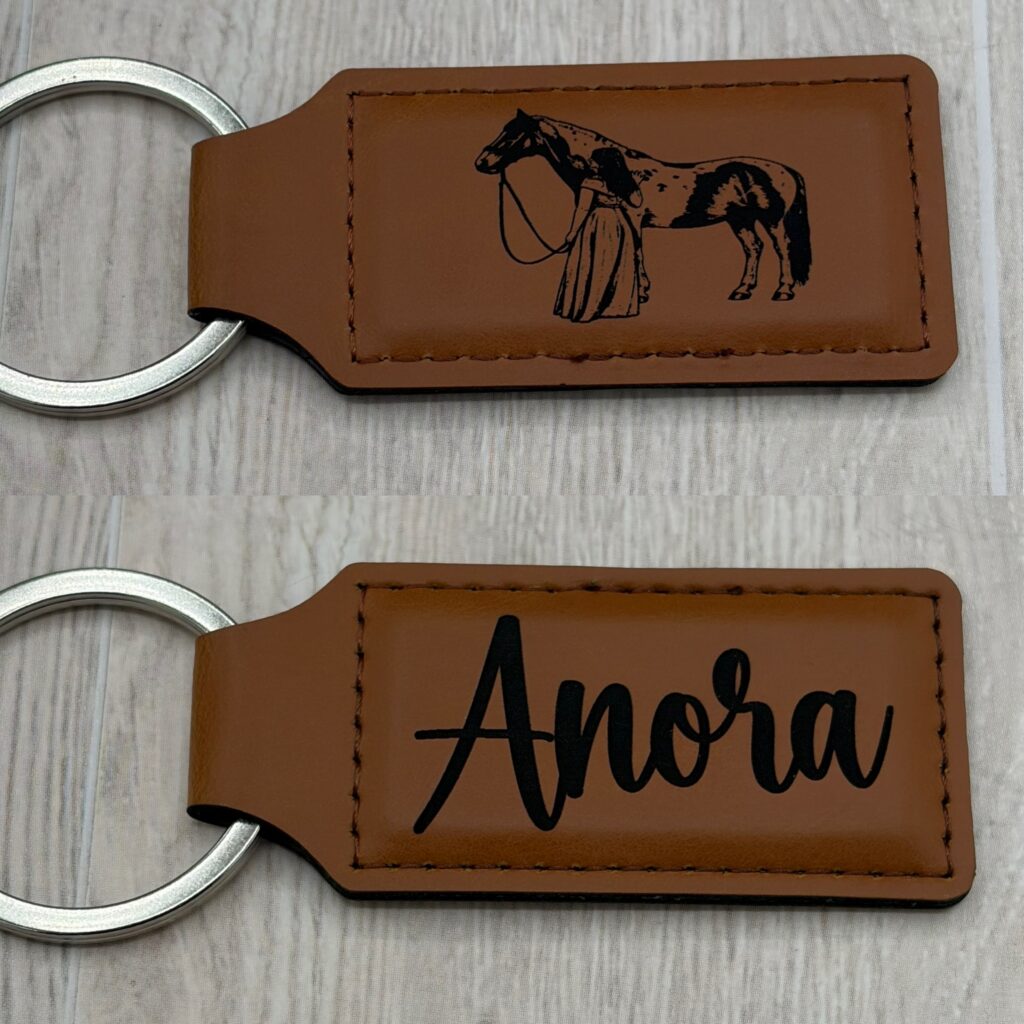 Two custom engraved leather keychains, one with a woman and horse design and one with the name Anora