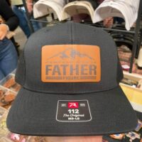 Black trucker hat with a Father Figure leather patch under a mountain range